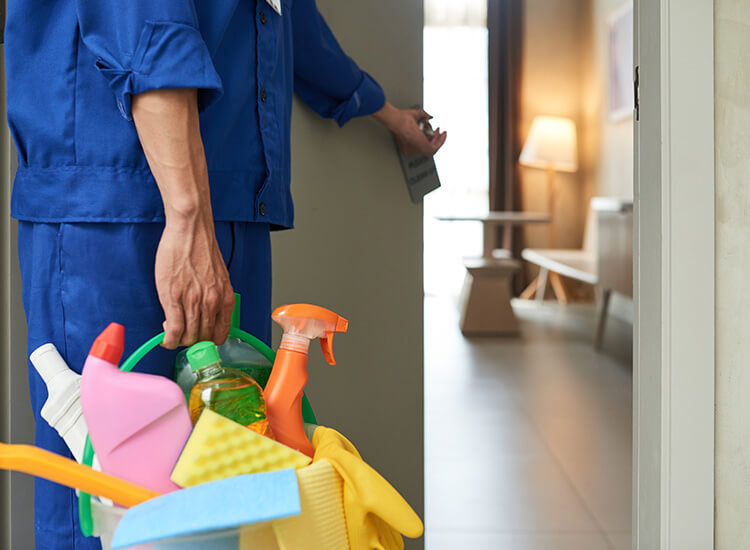 someone in a blue uniform opening a door and carrying the cleaning products.