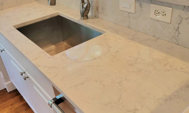 Elegant kitchen countertop with white marbled design, stainless steel sink, and modern brushed faucet, complemented by wooden flooring.