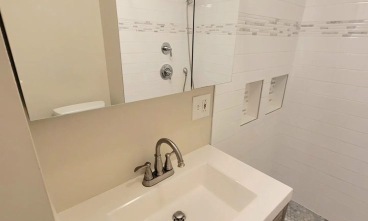 Modern bathroom interior with white subway tile walls, a hint of exposed brick, undermount sink with brushed nickel faucet, and clear glass shower partition.