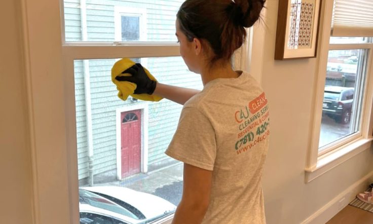 women wearing black gloves and a yellow cloth cleaning the window glass.