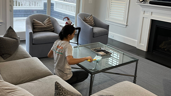 C4U professional cleaner polishing the glass coffee table while wearing a white shirt with the logo.