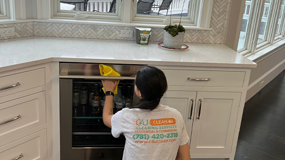 C4U professional cleaner polishing the glass of the beers fridge table while wearing a white shirt with the logo.