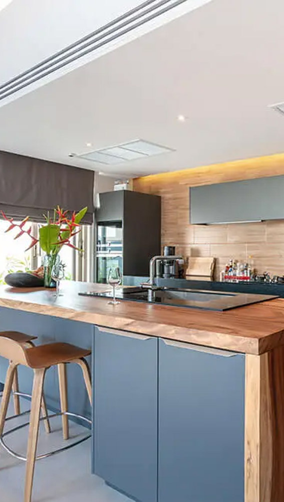 Modern kitchen interior with wooden countertops, blue cabinets, and pendant lighting.