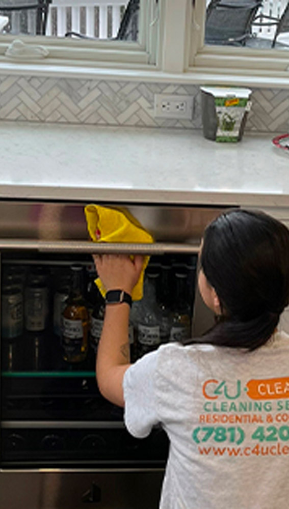 C4U professional cleaner polishing the glass of the beers fridge table while wearing a white shirt with the logo.