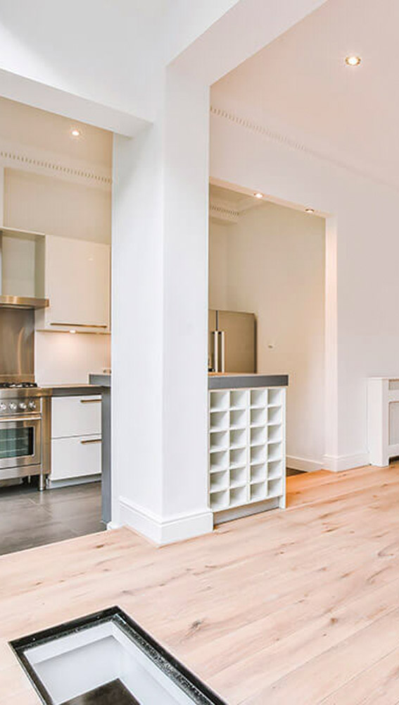 Modern kitchen interior with white cabinetry, wine rack, and light wooden flooring.