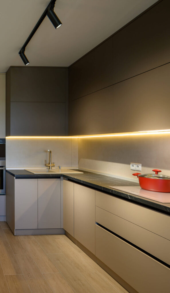 Modern kitchen design with muted gray cabinetry, under-cabinet lighting, and a red pot on the sleek countertop.