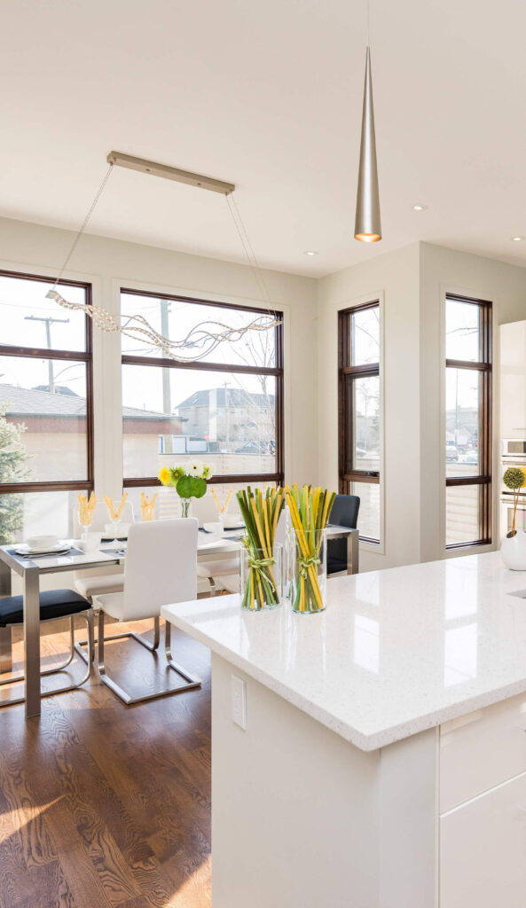 Bright dining area with a white table, modern chairs, pendant lights, and large windows offering a city view.